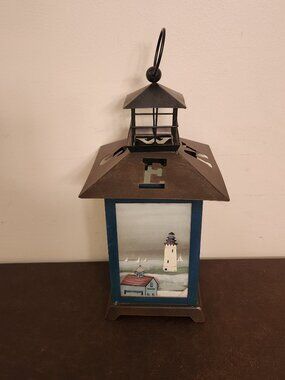 Nautical themed decorative candle holder features a lighthouse or sailboat